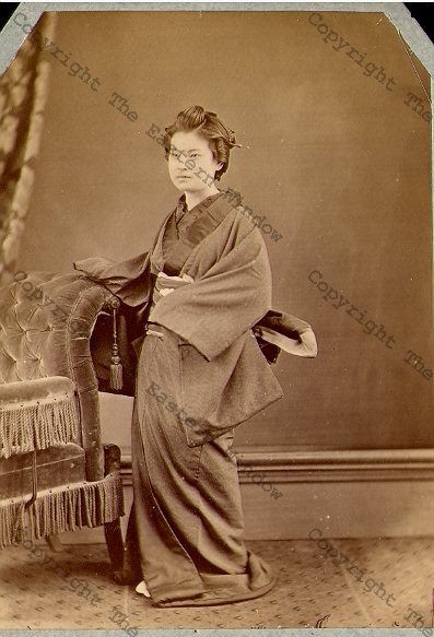 Geisha in traditional dress besides a Western style chair - 1870's albumen